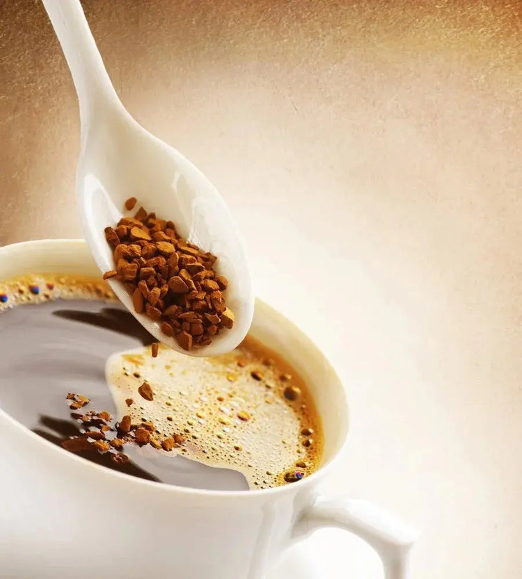 White spoon adding instant coffee granules to a fresh cup of black coffee with froth