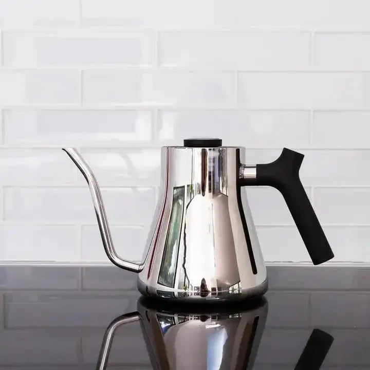 Stainless steel stovetop pour-over kettle with black ergonomic handle on reflective black surface